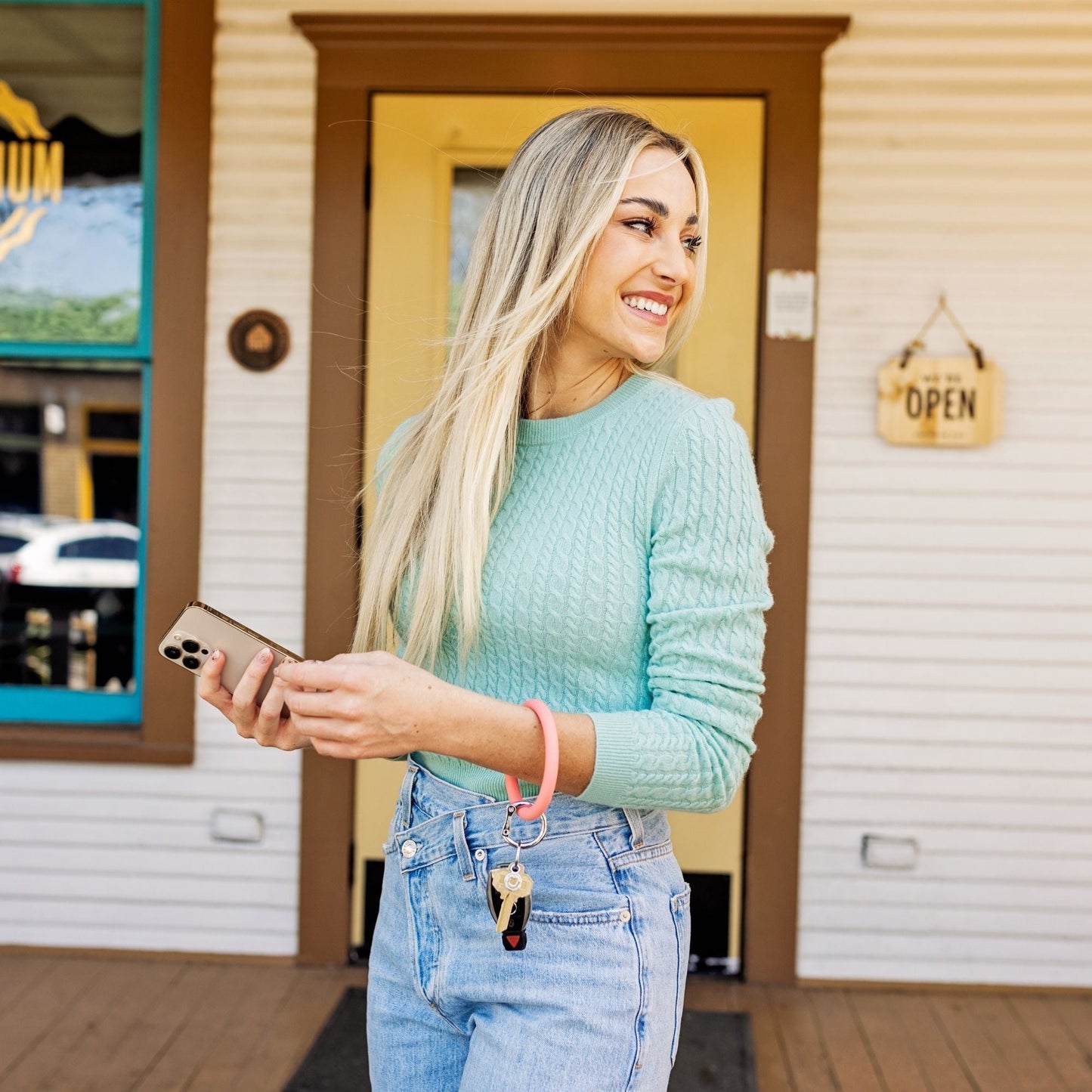 Woman wearing the Coral Reef Signature Silicone Big O Key Ring with attached keys and car fob while holding a smartphone outdoors.