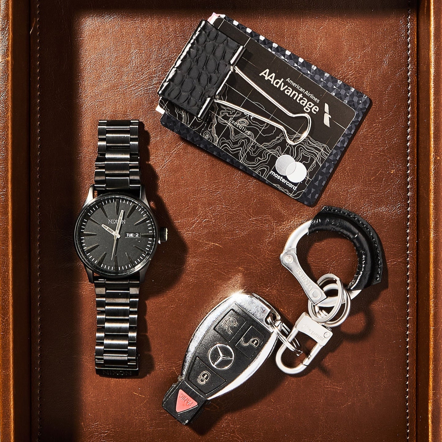 Watch, cardholder, and keychain set on a brown leather surface