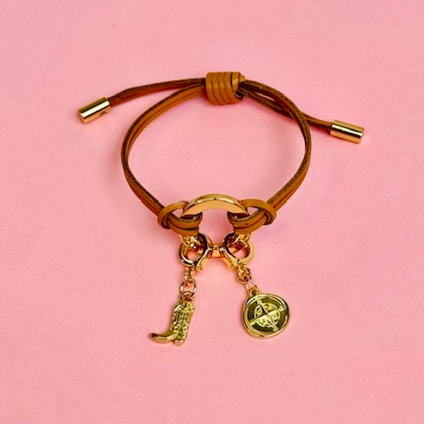 Brown leather bracelet with gold charms on a pink background