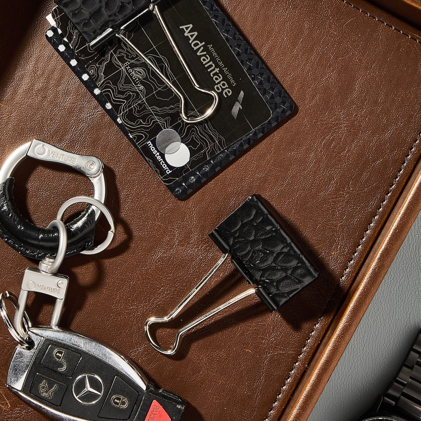 Keychain, cardholder, and paper clip on a brown leather surface