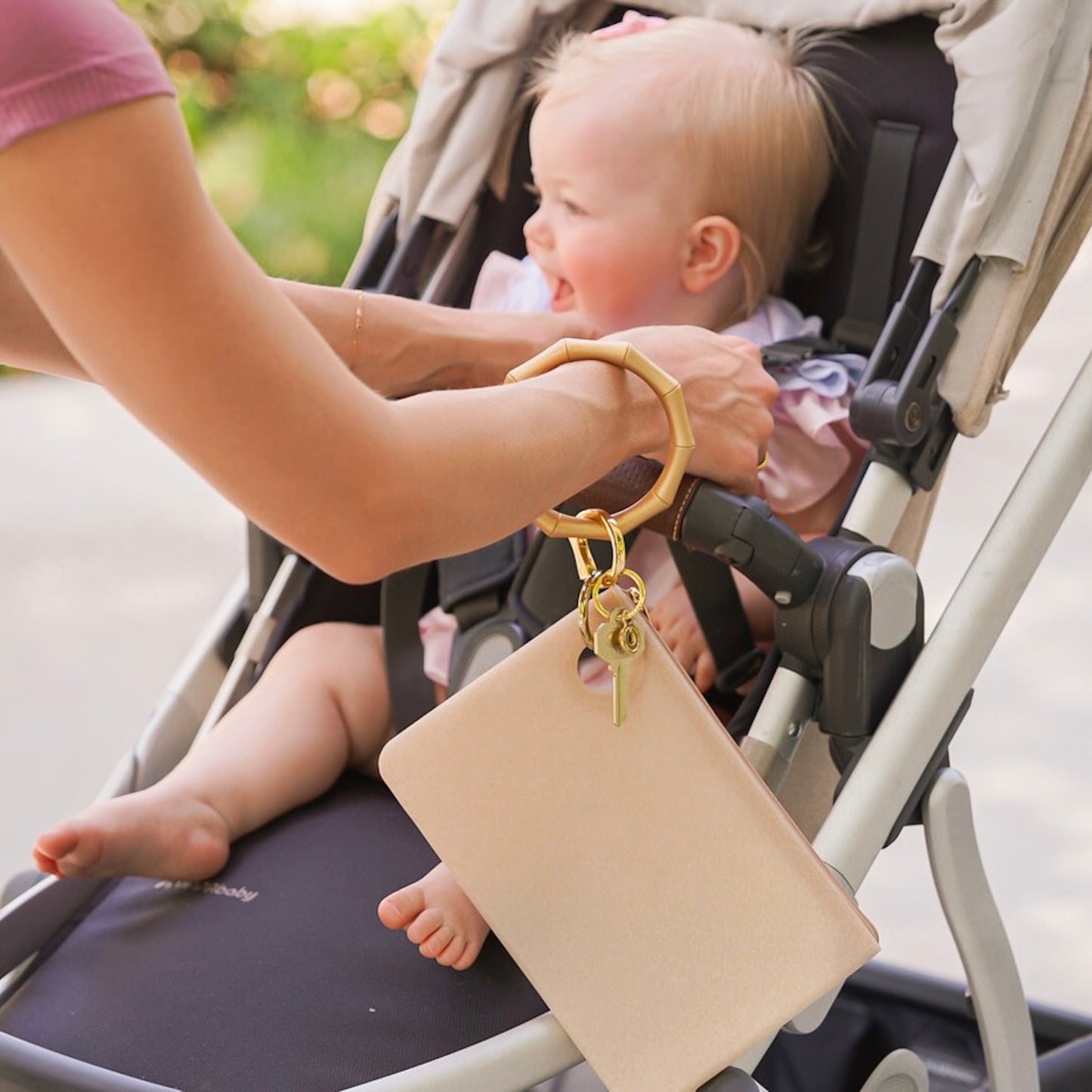 Mom putting child in stroller while wearing gold large wristlet wallet 