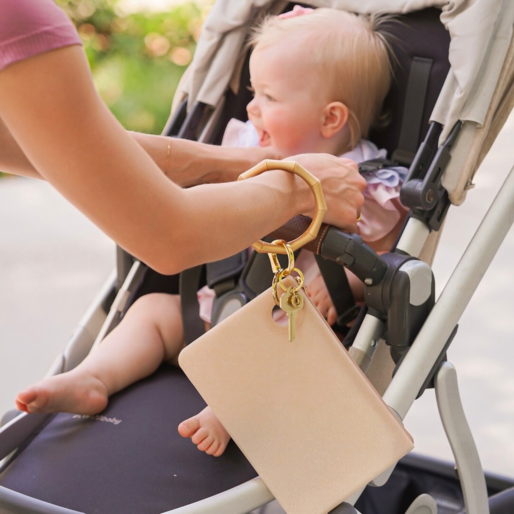 Mom putting child in stroller while wearing gold large wristlet wallet 