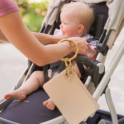Mom putting child in stroller while wearing gold large wristlet wallet 