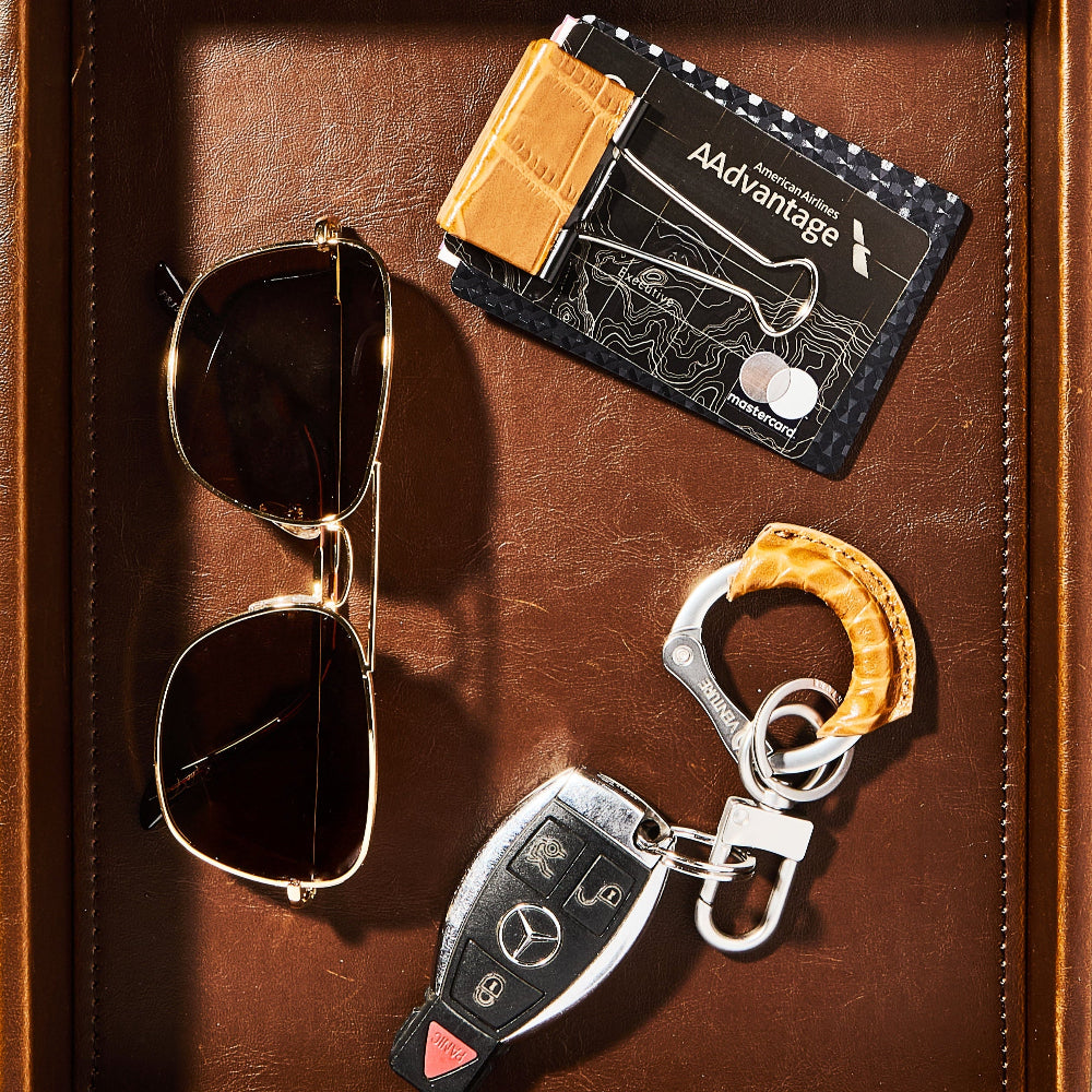 Sunglasses, cardholder, and keychain on a brown leather surface