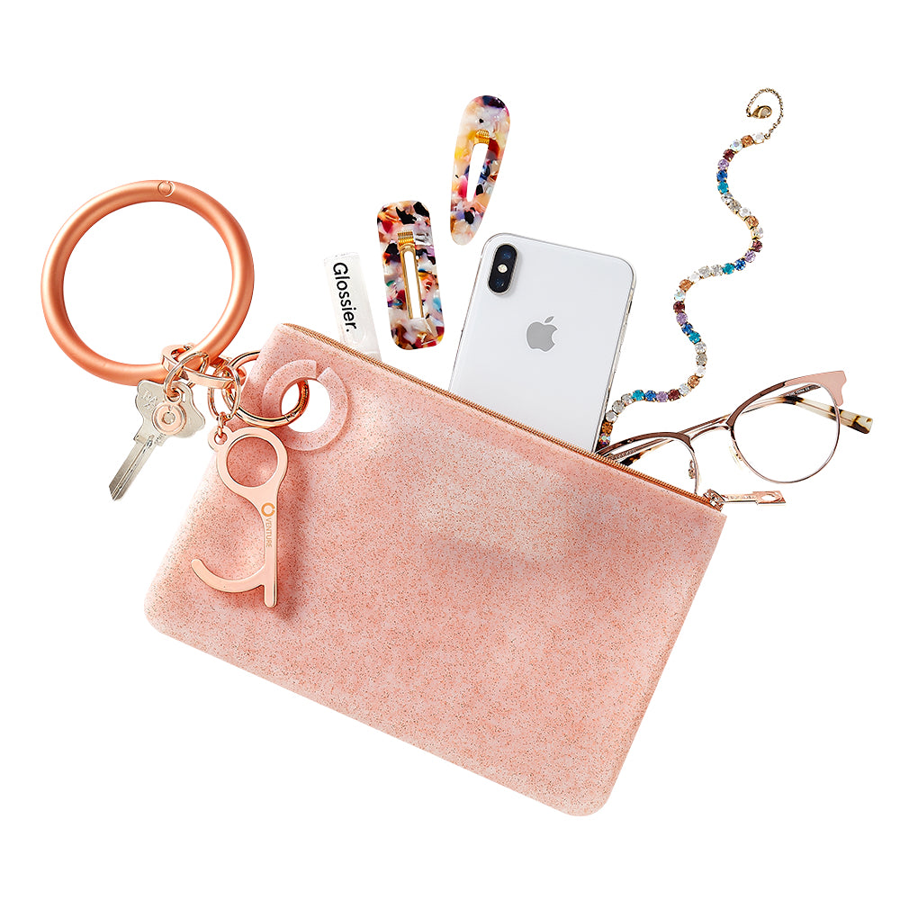 Large silicone rose gold confetti pouch attached to solid rose gold big o key ring with hair accessories and glasses coming out of the top