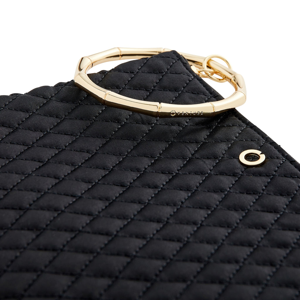 Close up of black quilted bracelet bag with gold bamboo handle