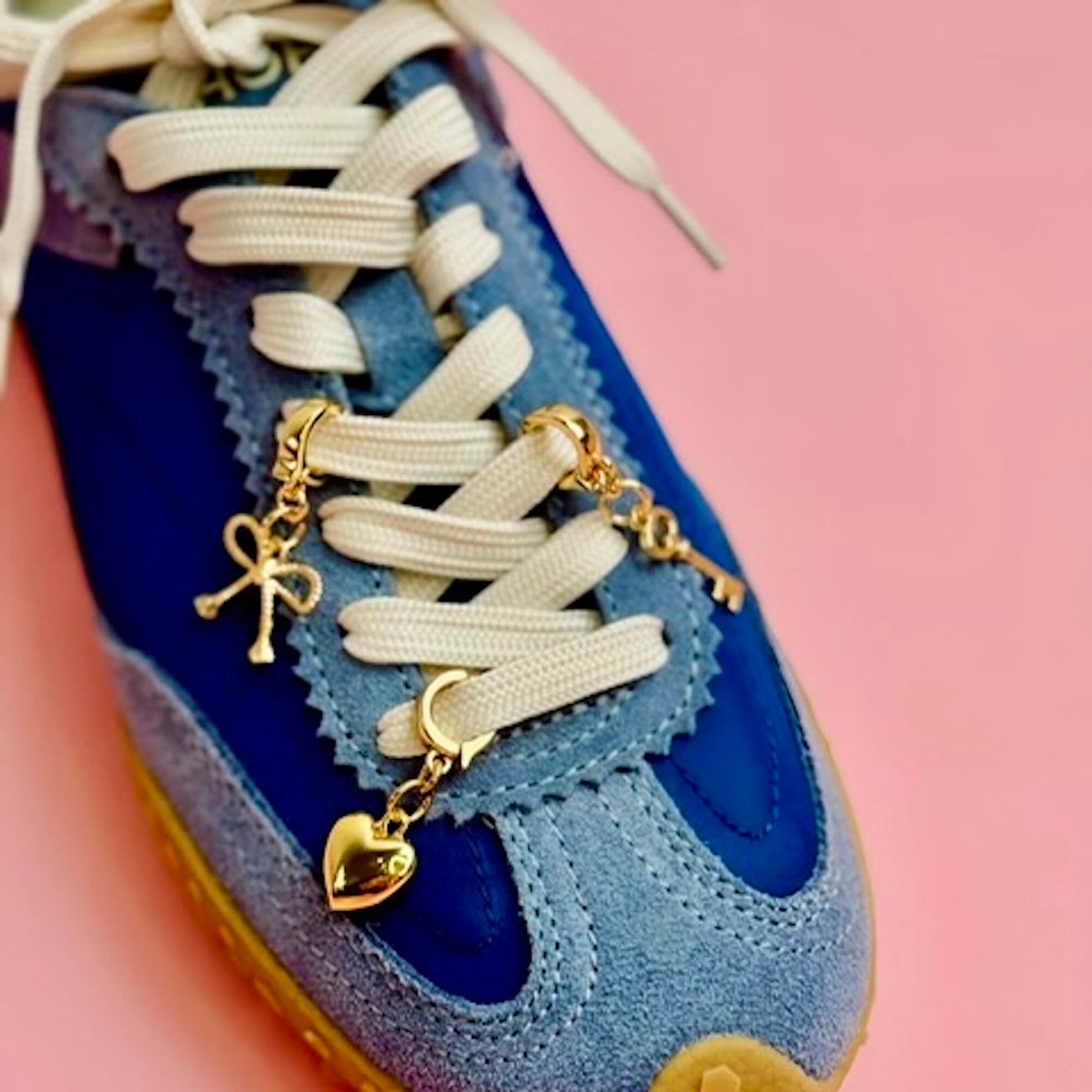 Blue sneaker with gold heart, key and bow charm on a pink background