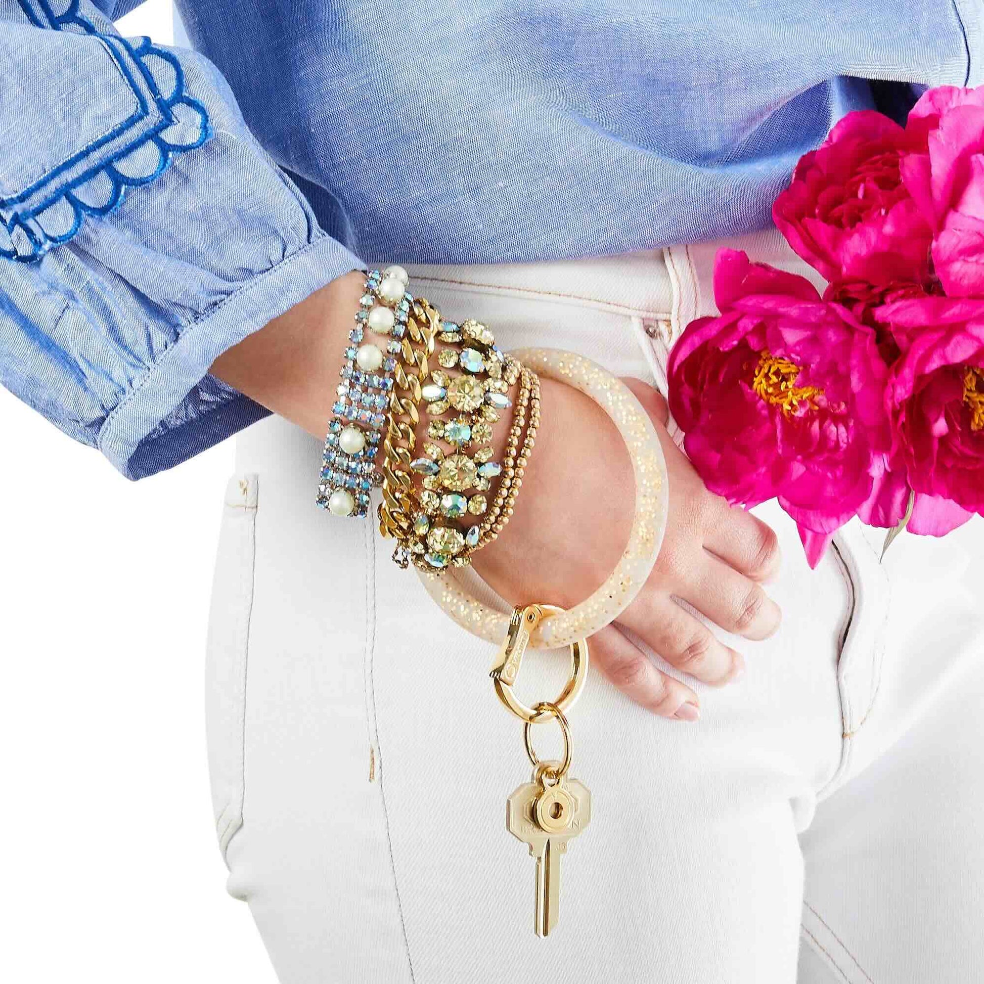 Close-up of a hand wearing multiple bracelets with a keychain, against a background of pink flowers.