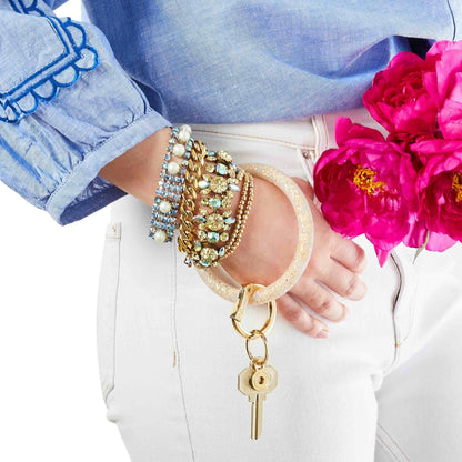 Close-up of a hand wearing multiple bracelets with a keychain, against a background of pink flowers.