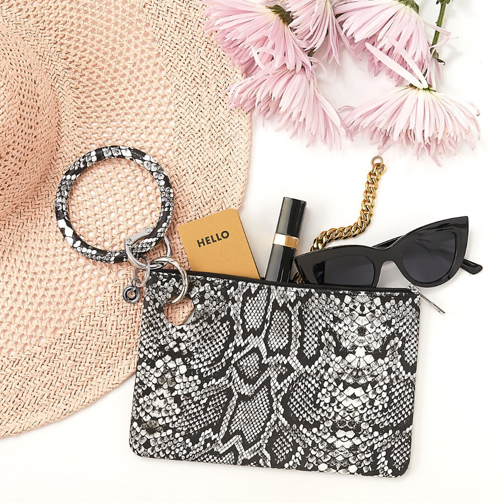 Snakeskin-patterned pouch with accessories including a hat, flowers, and sunglasses on a white background