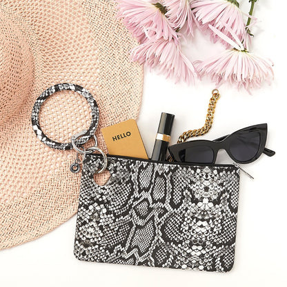 Snakeskin-patterned pouch with accessories including a hat, flowers, and sunglasses on a white background
