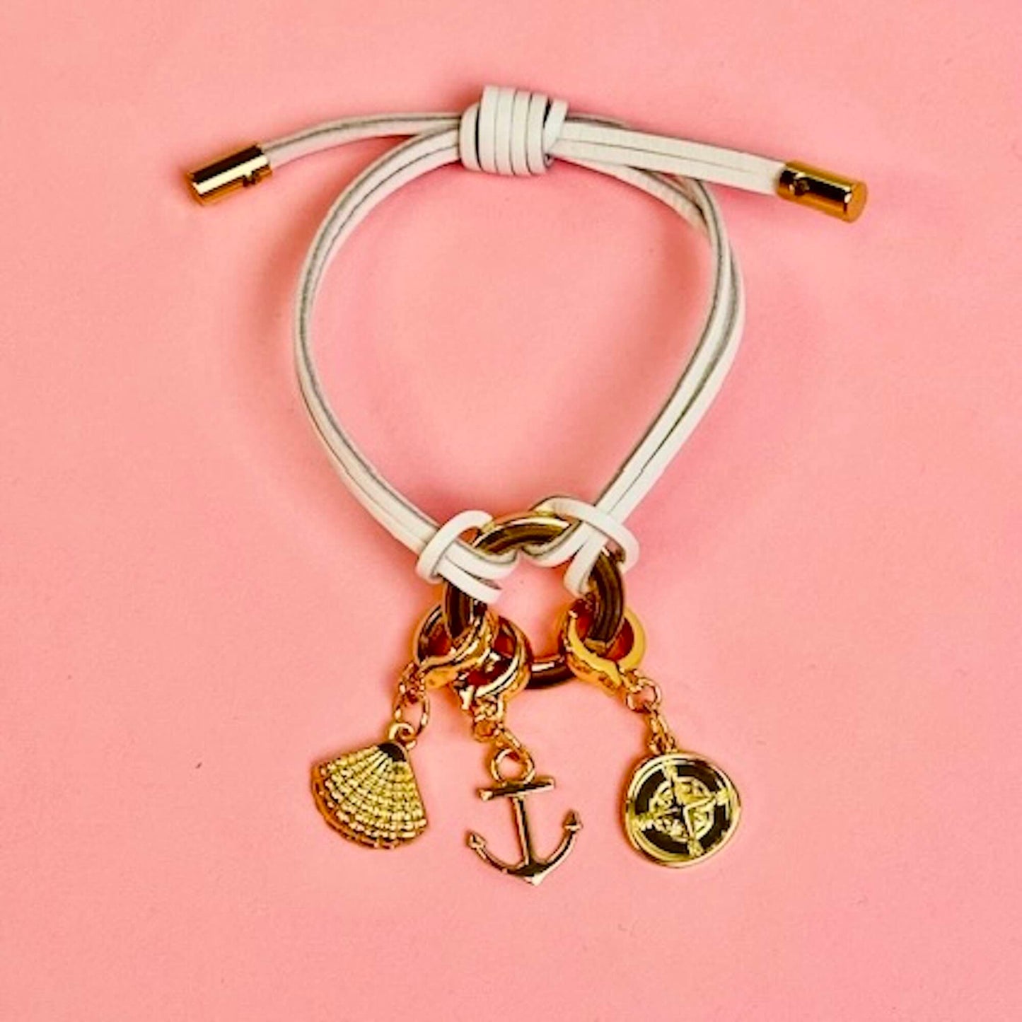 White leather bracelet with a shell charm, anchor charm and compass charm attached.