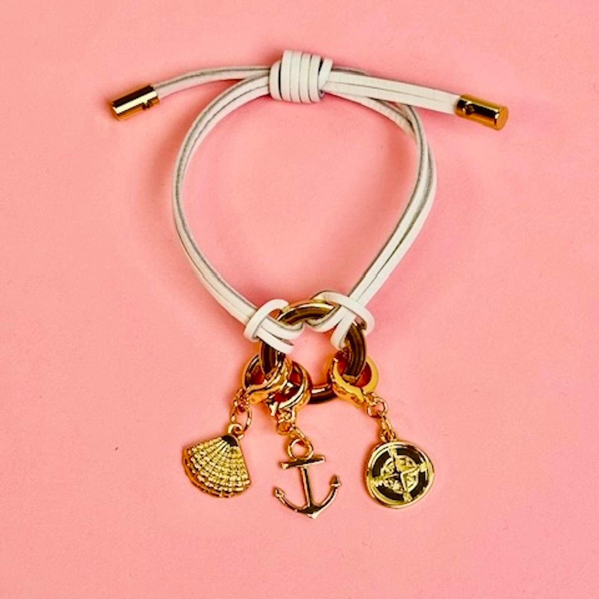 White leather bracelet with a shell charm, anchor charm and compass charm attached.