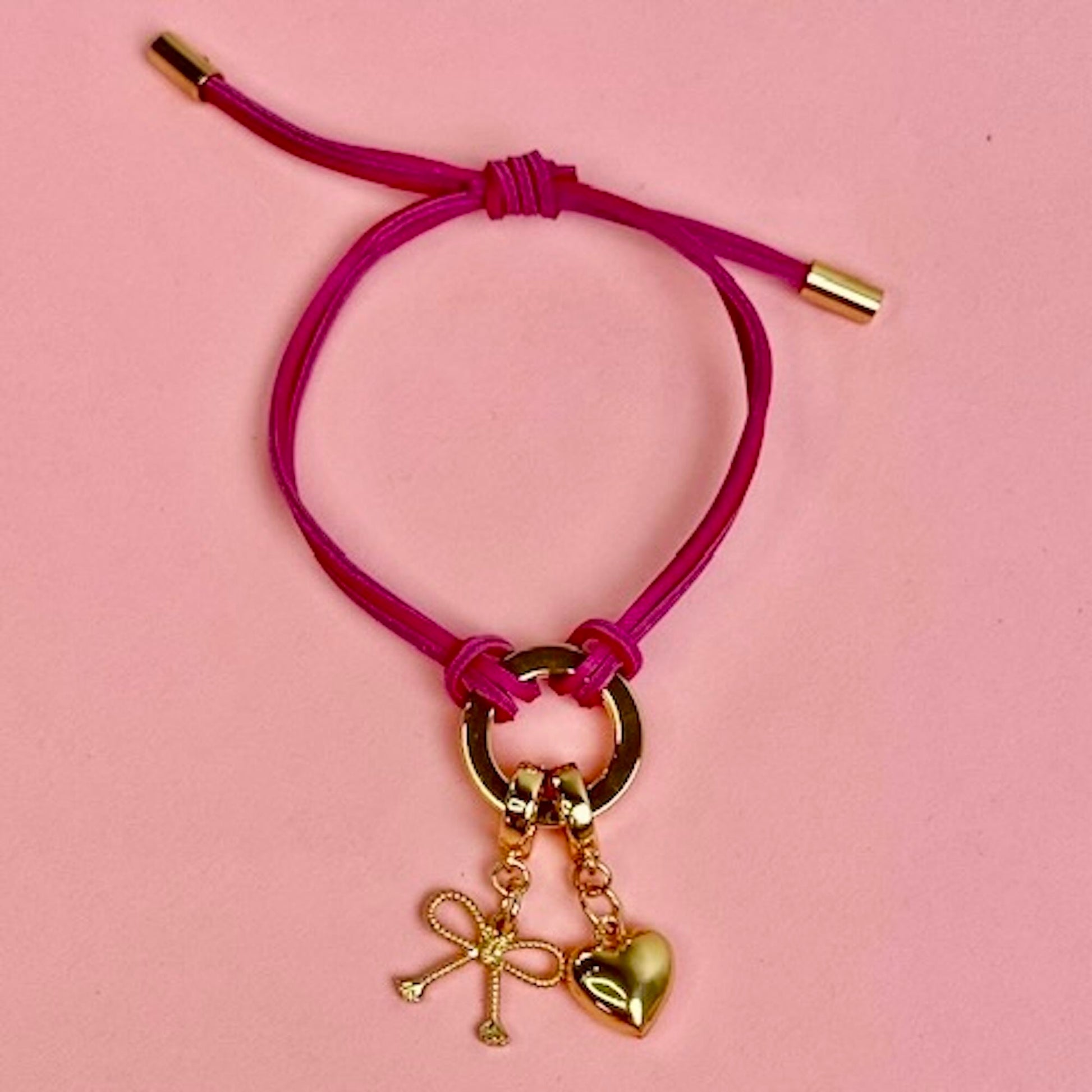 Pink bracelet with gold charms on a pink background