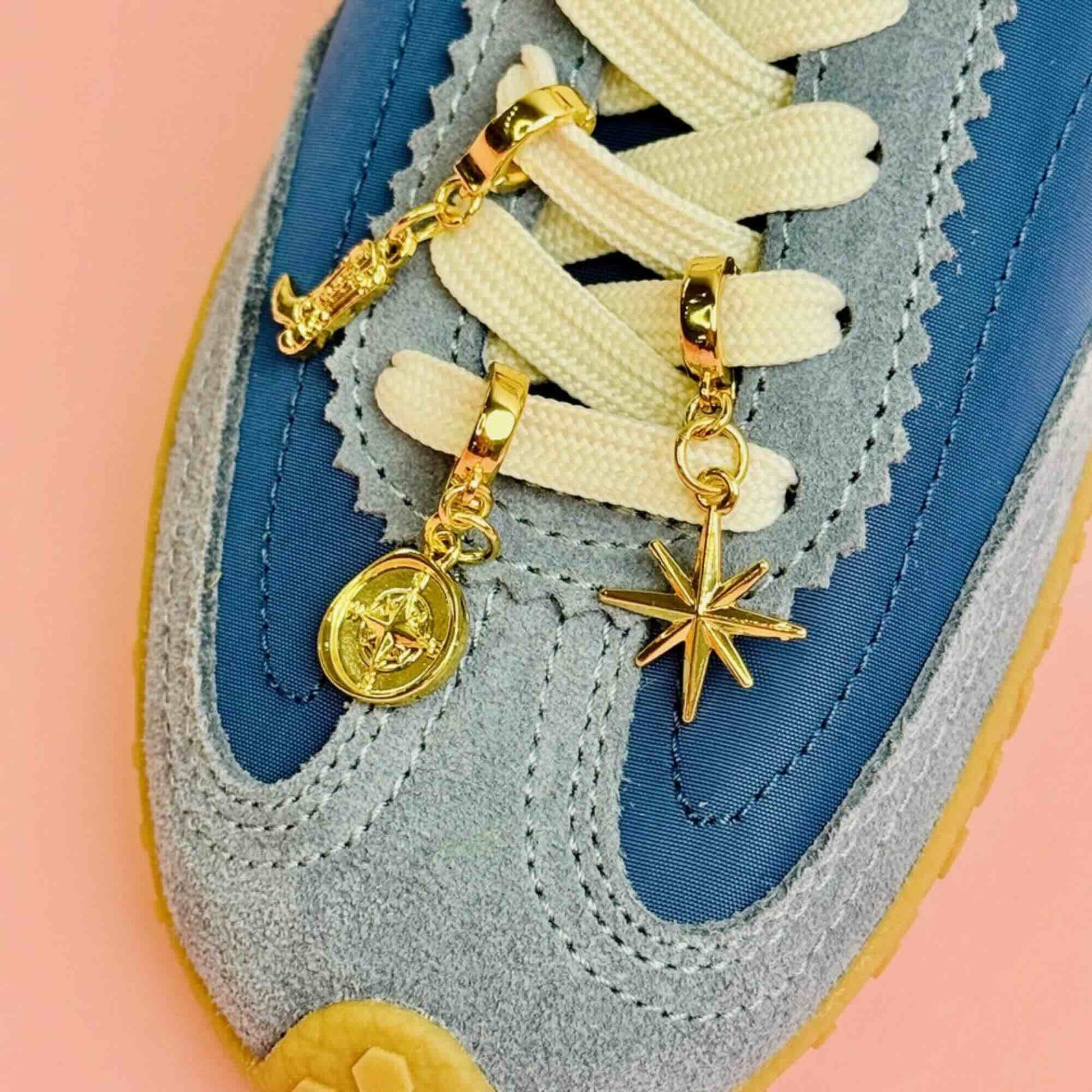 Gold charms in a cowboy boot, compass and star attached to the laces of blue sneakers 