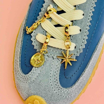 Gold charms in a cowboy boot, compass and star attached to the laces of blue sneakers 