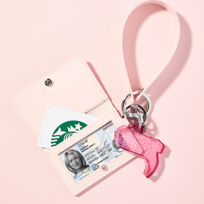 Light pink ID case with a clear ID window and Starbucks card, attached to a pink leather wristlet strap with a pink acrylic cowboy boot keychain and silver hardware, styled on a pastel pink background.