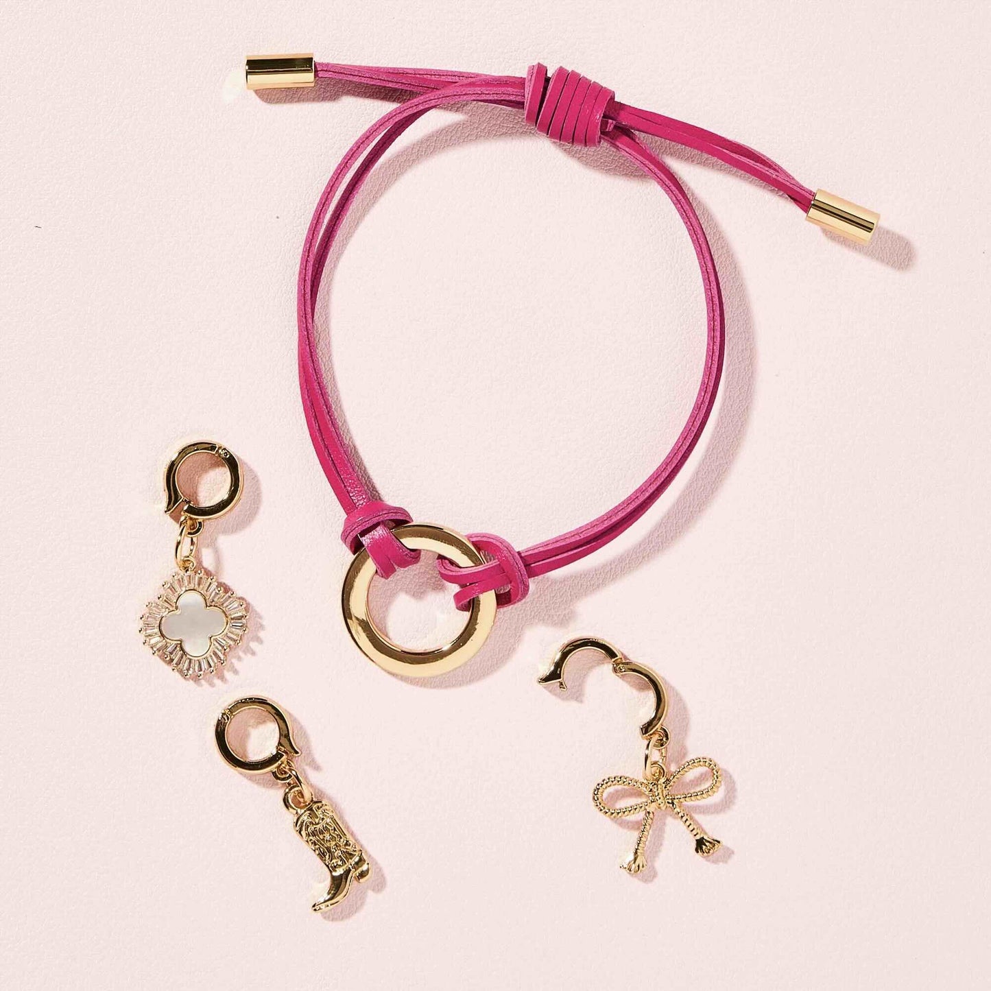 Pink bracelet with gold charms on a light pink background