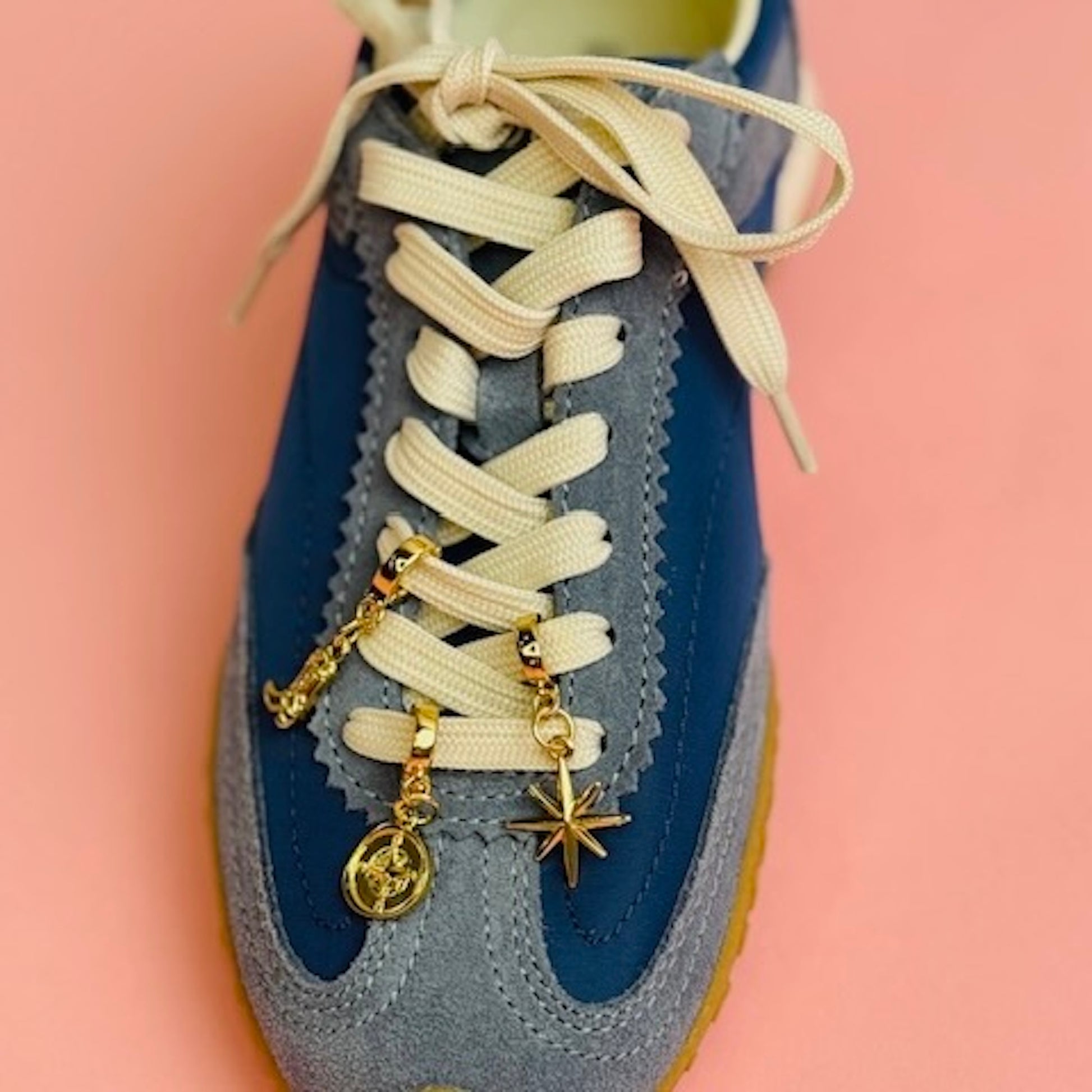 Blue sneaker with a cowboy boot, compass and star gold charms on the laces. 