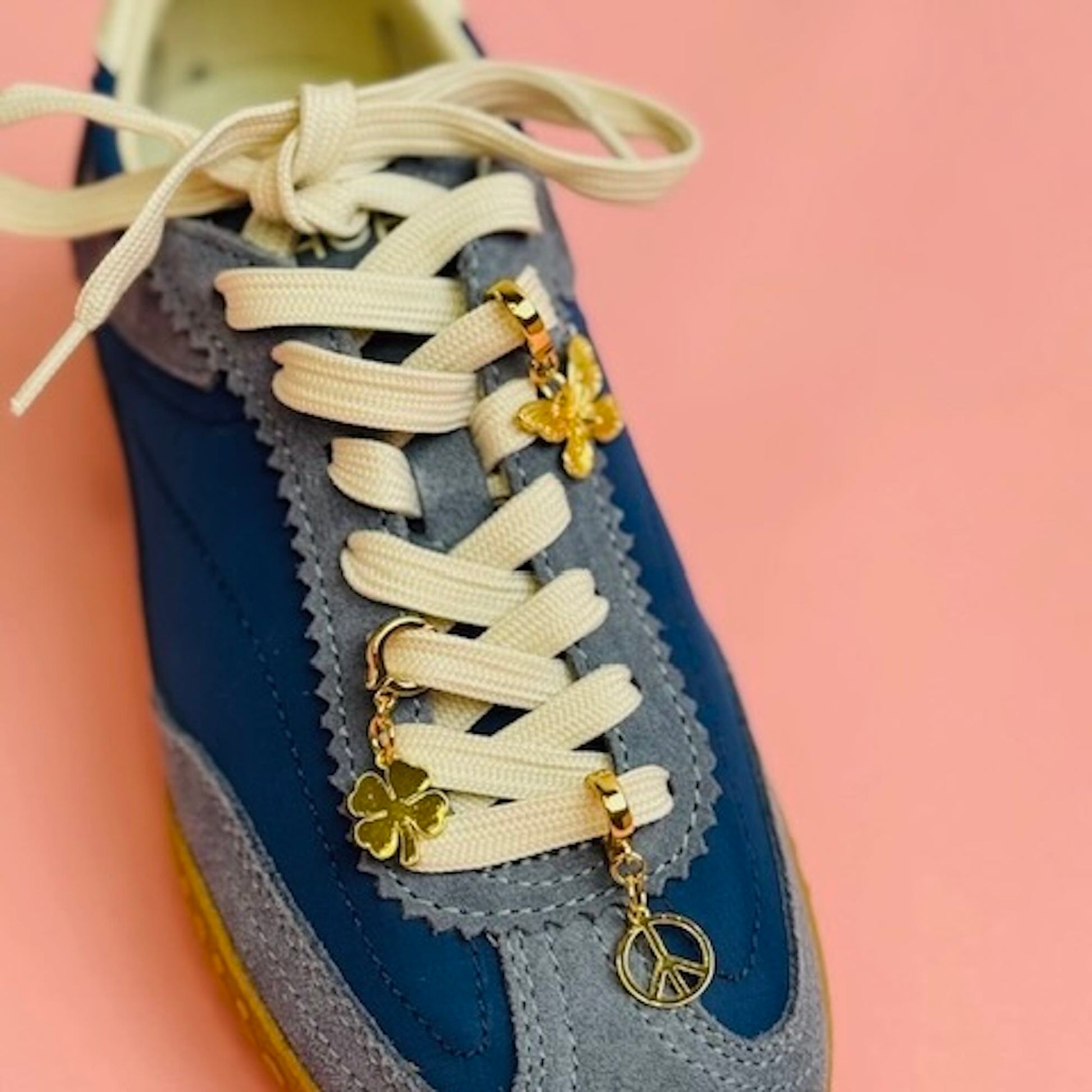 Blue sneaker with white laces and a butterfly, peace sign and clover gold charm attached