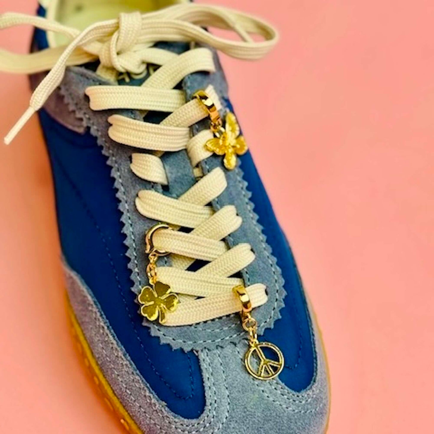 Blue sneaker with white laces and a butterfly, peace sign and clover gold charm attached
