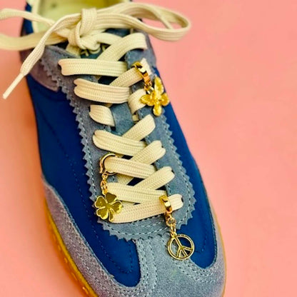 Blue sneaker with white laces and a butterfly, peace sign and clover gold charm attached
