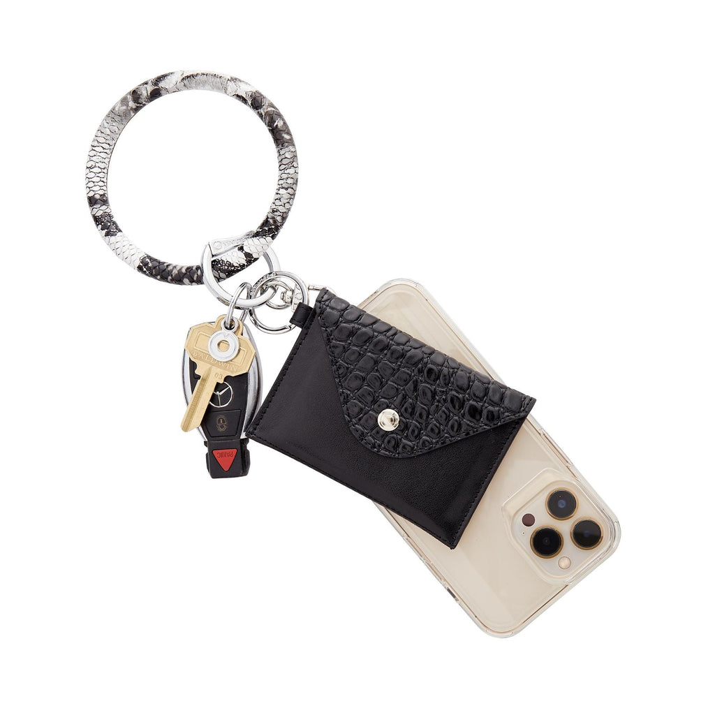 Quicksilver - The Hook Me Up™ Universal Phone Connector - Oventure with a big o key ring in tuxedo snakeskin embossed leather. The phone is attached to the key ring along with a mini envelope wallet in black leather