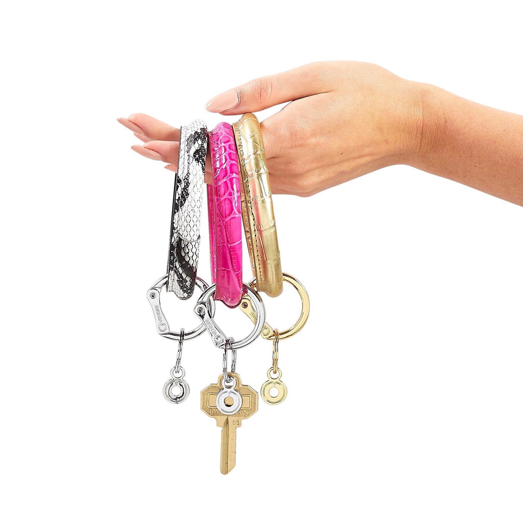 Black and white embossed snakeskin print leather Big O Key Ring with silver locking clasp held next to Pink Topaz Croc and Solid Gold Rush Croc