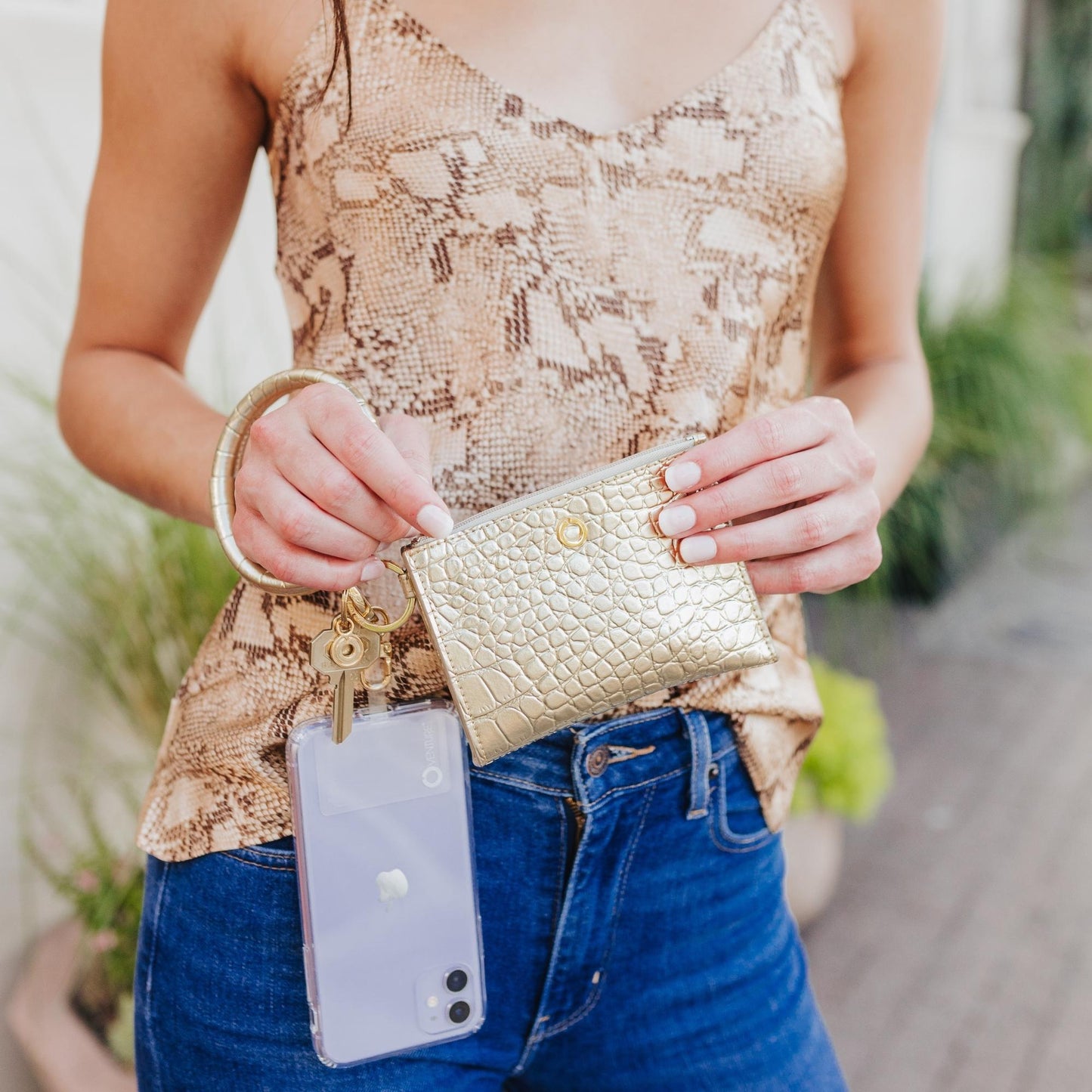 Gold wallet wristlet with phone holder for organization shown with key ring bracelet and phone case attached.